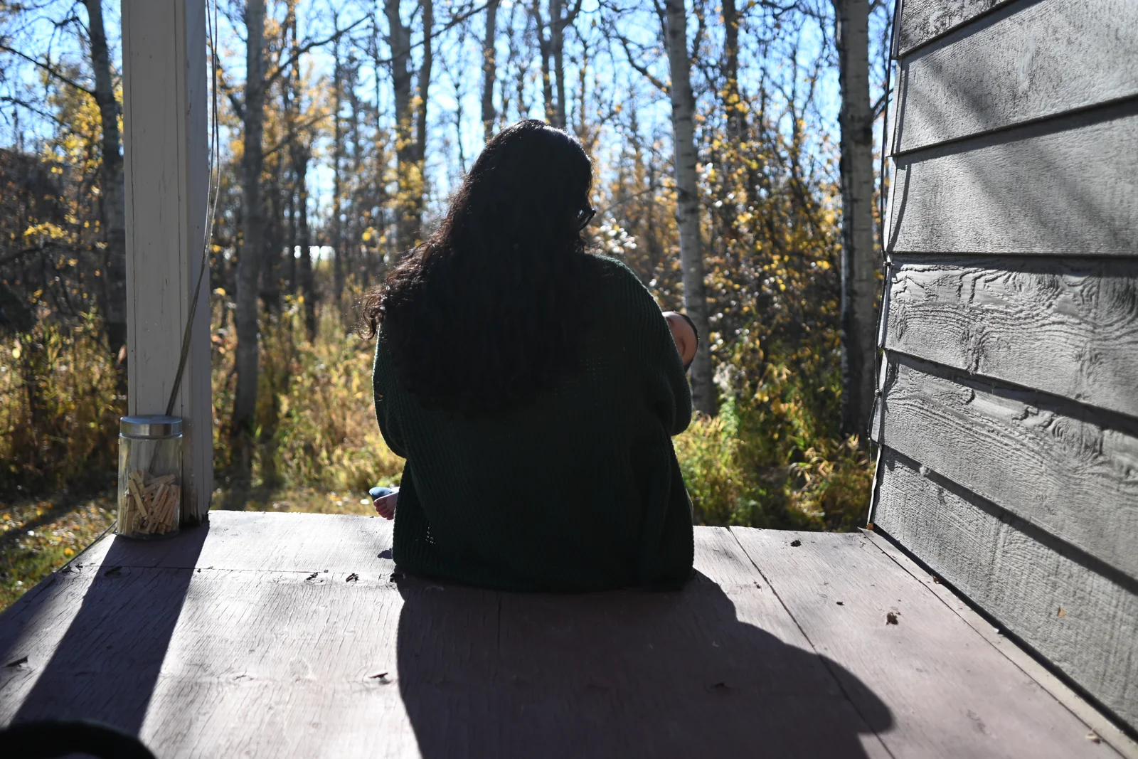 Kacy sitting quietly on a porch looking toward the woods.